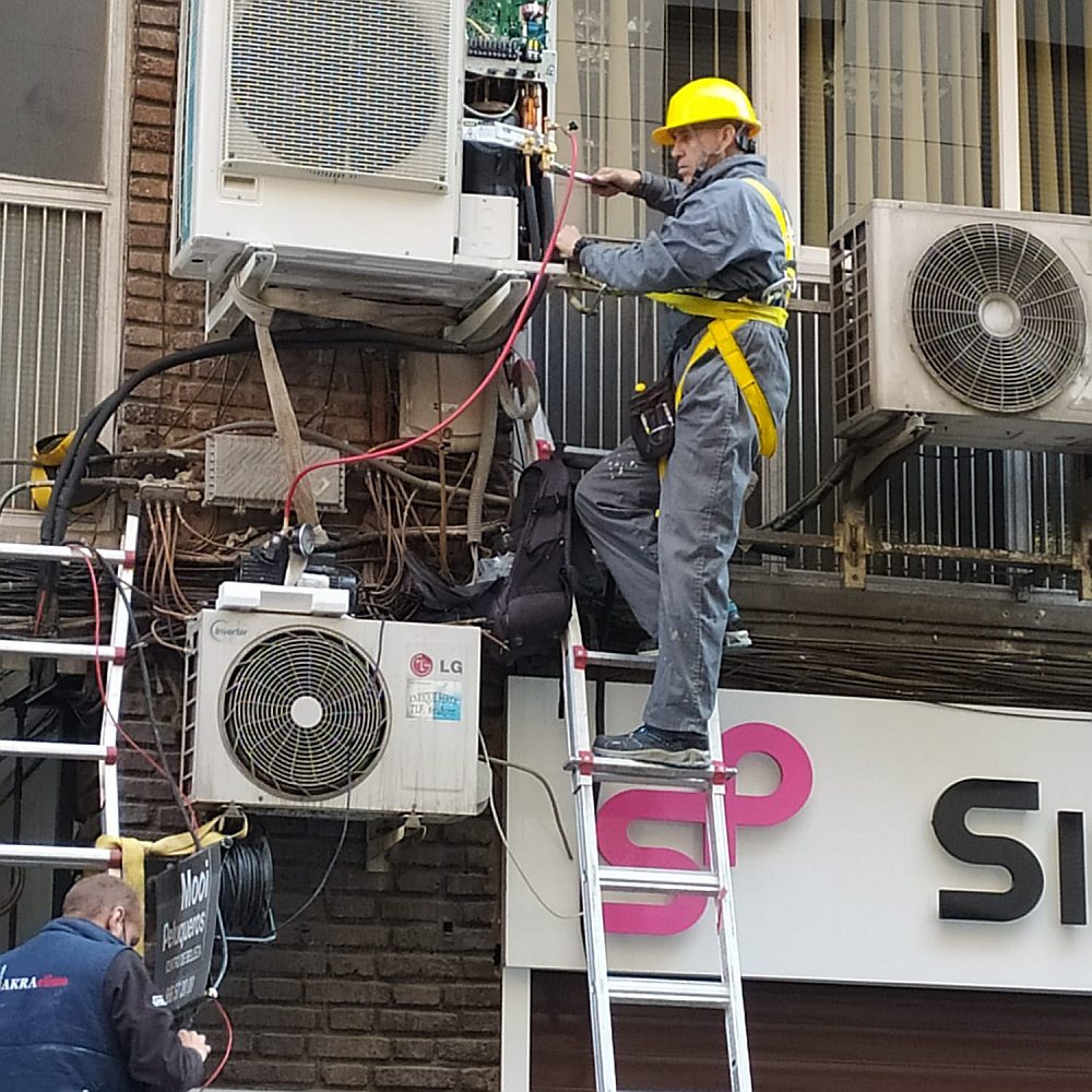 Técnico con casco y arnés de seguridad instalando un split en fachada